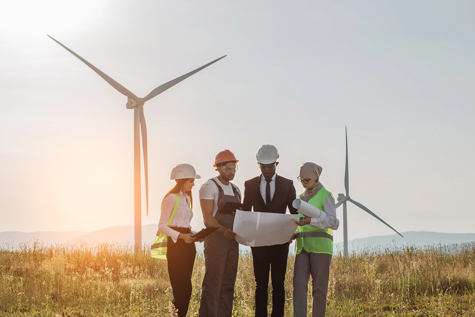Ingenieure und Berater diskutieren Baupläne vor Windkraftanlagen, Symbol für Recruiting in Renewable Energy